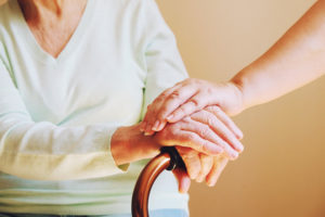 Younger person resting hand on hand of seated elderly woman with cane