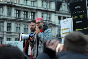 Christopher Wylie at outdoors protest speaking into megaphone