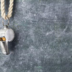 Silver whistle hanging on cord in front of chalkboard