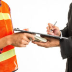 Man in business suit signing on clipboard held by construction worker while surreptitiously exchanging cash