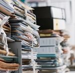 Disorganized paper records stacked on table