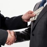 businessmen shaking hands and other placing money in others pocket