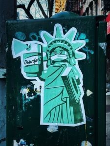 statue of liberty spraying disinfectant with a mask over her mouth