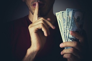 man holding money in hand and another hand with one finger over mouth