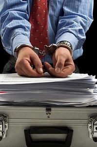 person handcuffed with hands on stack of papers with briefcase